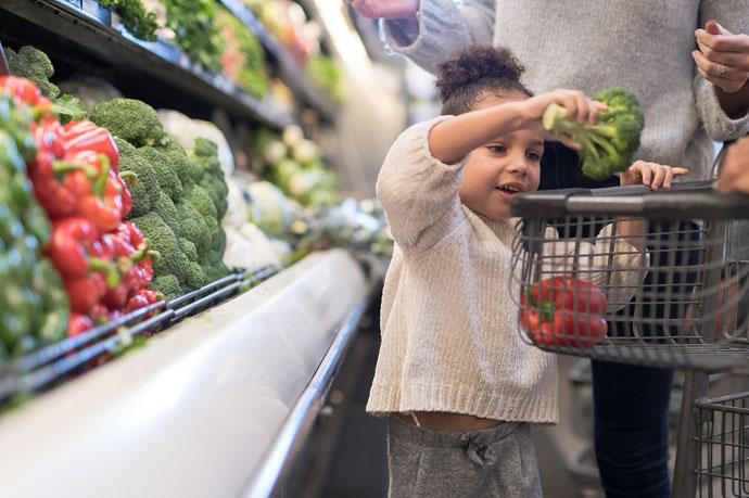 Child in supermarket trolley picking vegetables